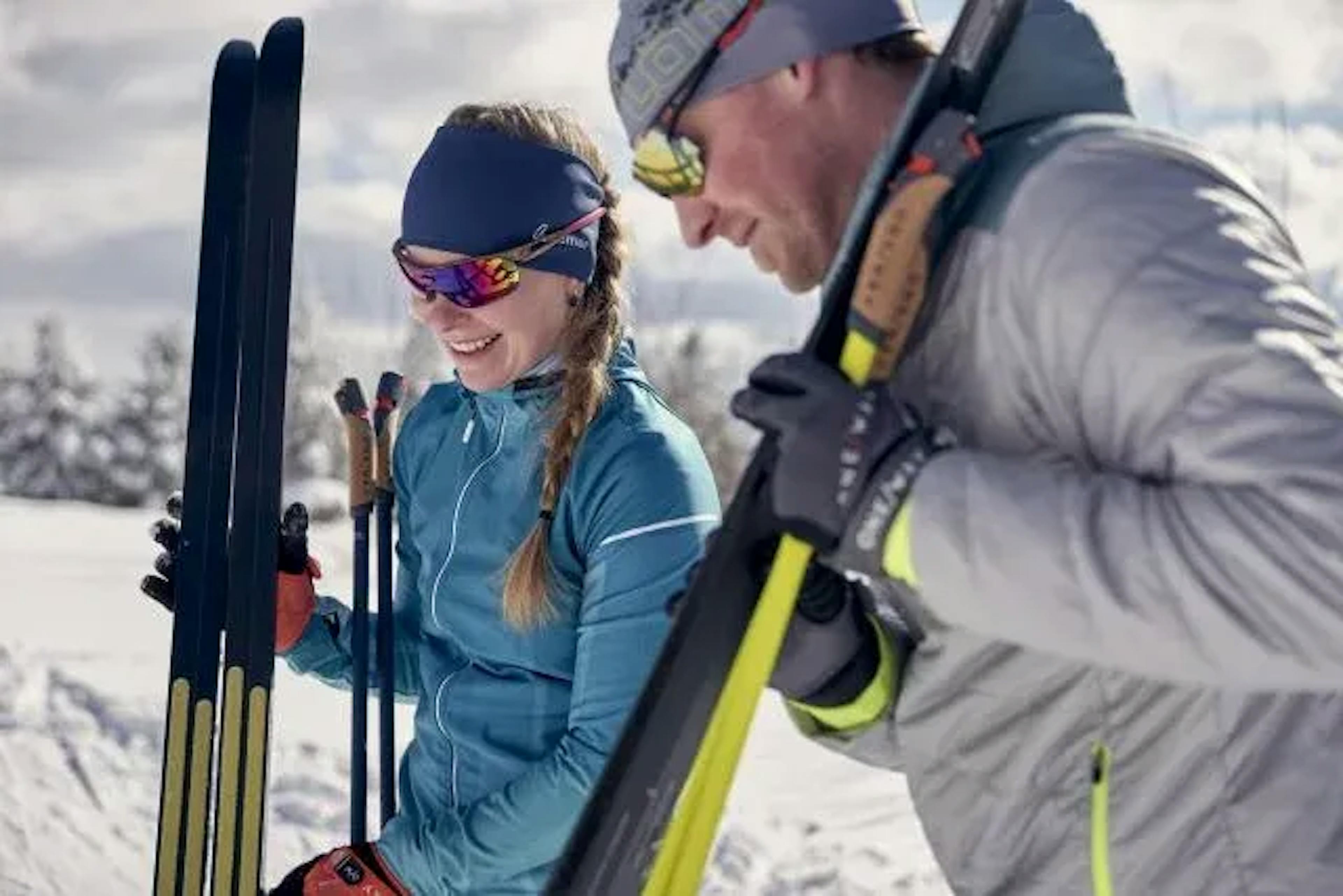 Esqui cross-country em Zermatt: Dois esquiadores riem ao vestir os esquis no inverno em caminhos cobertos de neve.