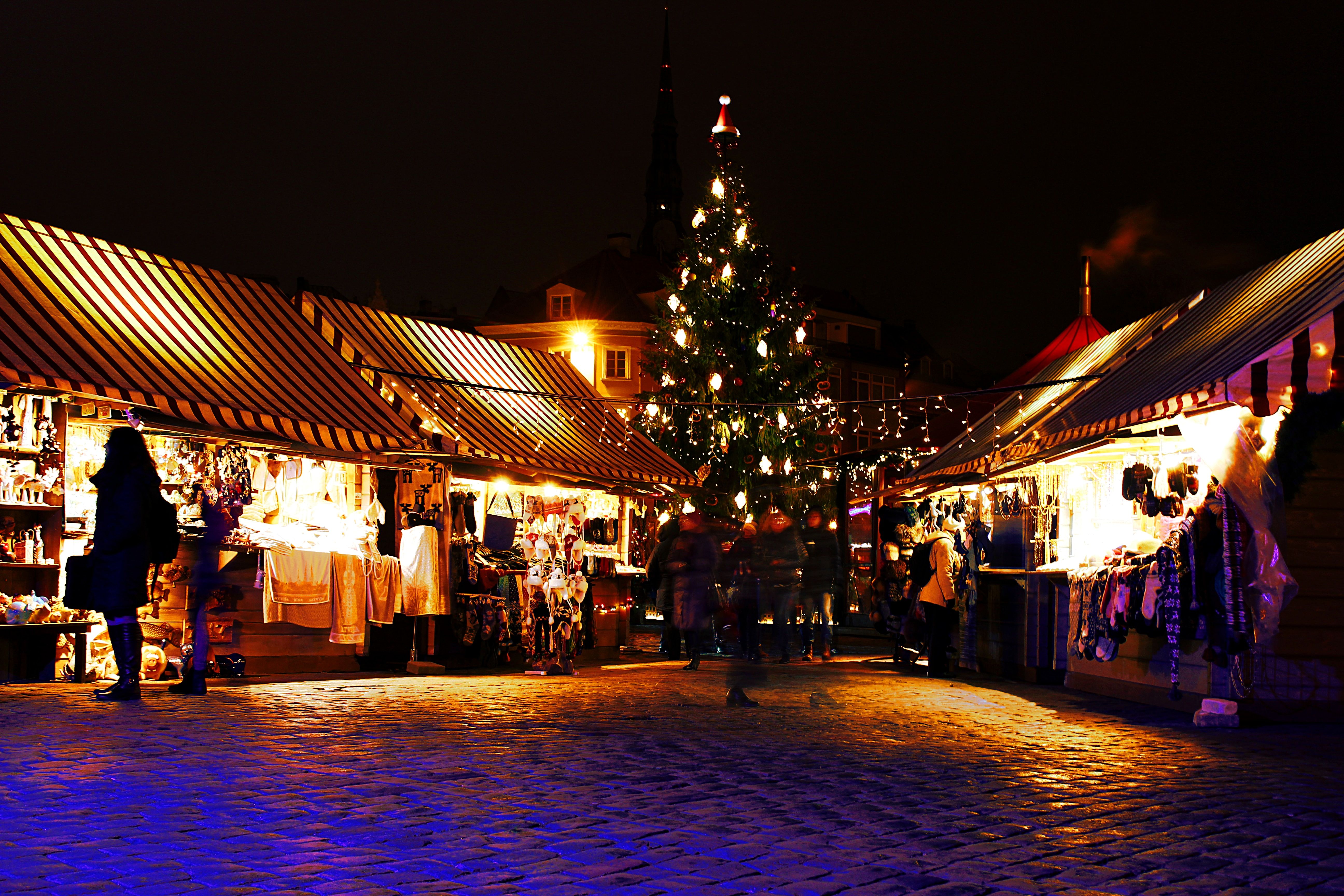 Weihnachtsmarkt mit festlich geschmücktem Baum, Ständen und bunten Lichtern in winterlicher Atmosphäre.