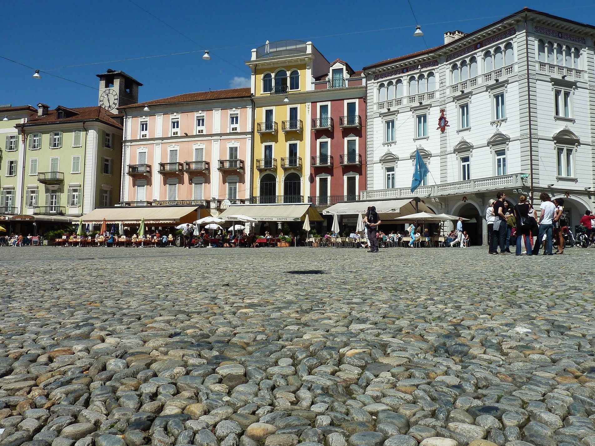 Locarno: Historischer Platz mit bunten Gebäuden und fröhlichen Menschen im Sommer.
