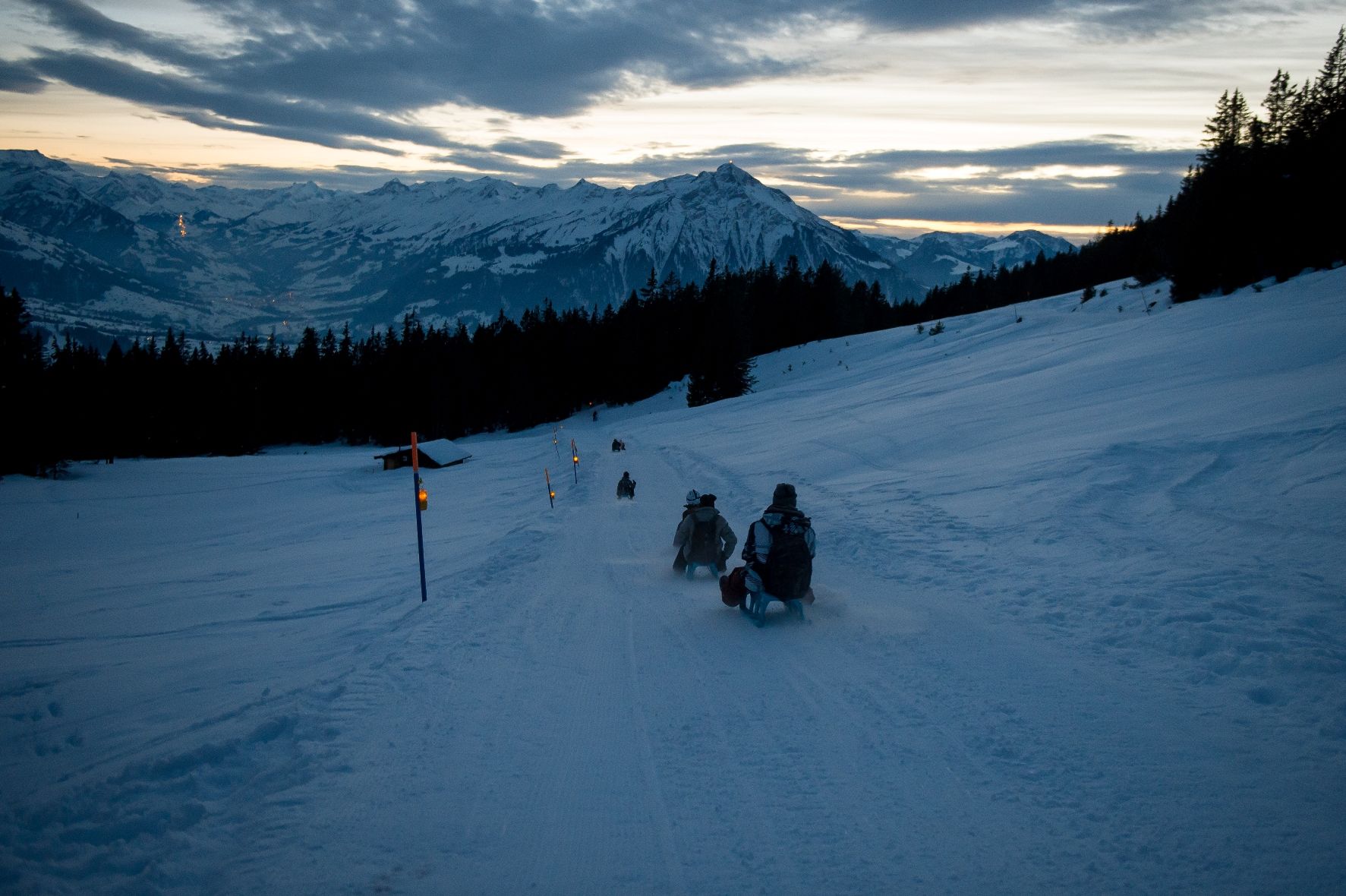 Hvězdné sáňky Niederhorn se sněhem a horským panoramatem při večerní soumraku.