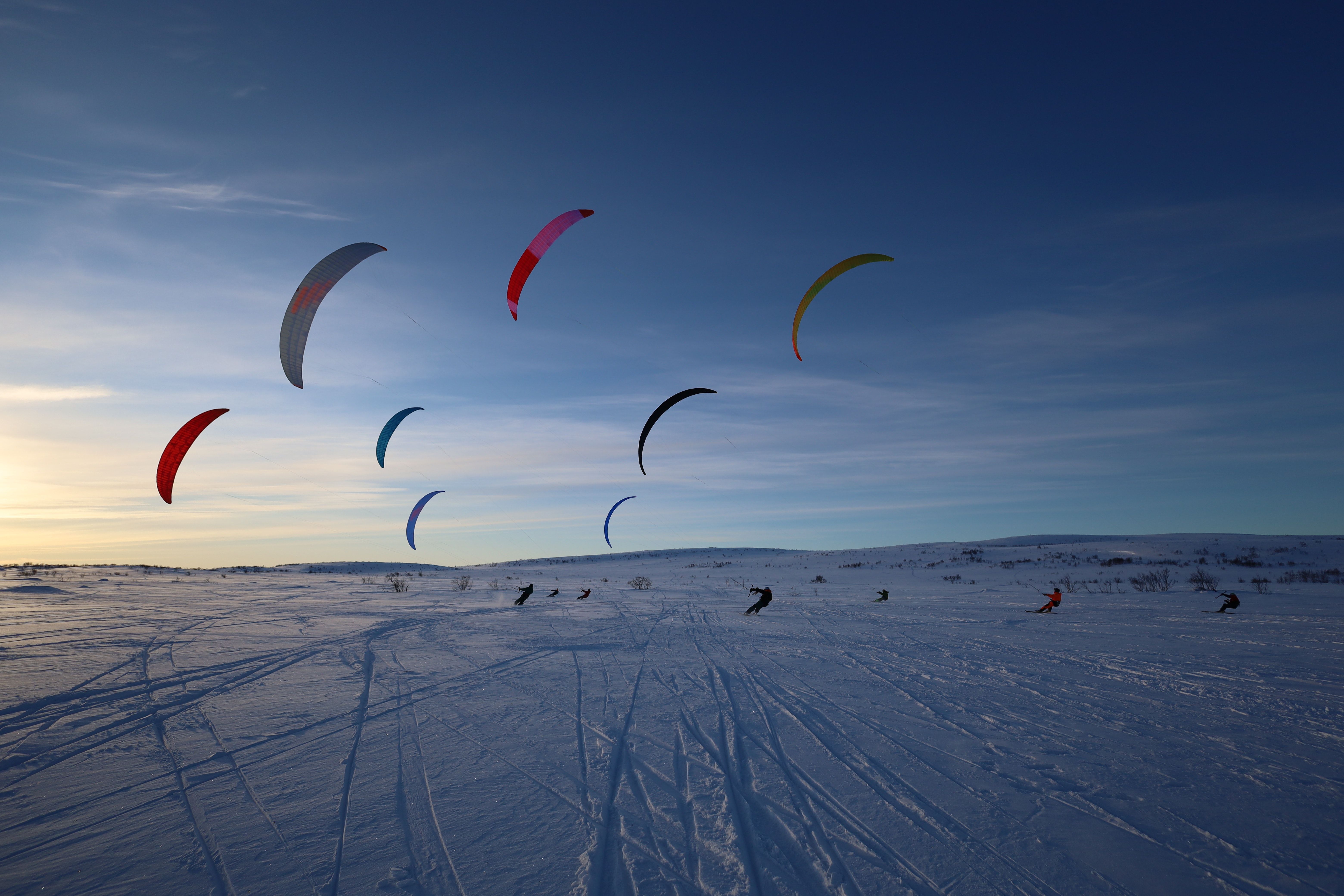 Snowkiting en invierno con cometas de colores en un área nevada bajo un cielo despejado