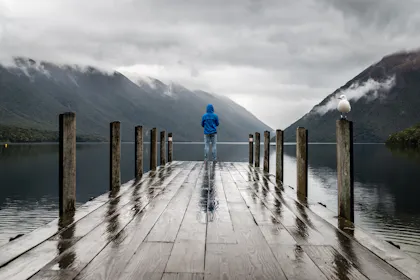 Wanderer auf Steg vor spiegelndem Wasser und Bergen
