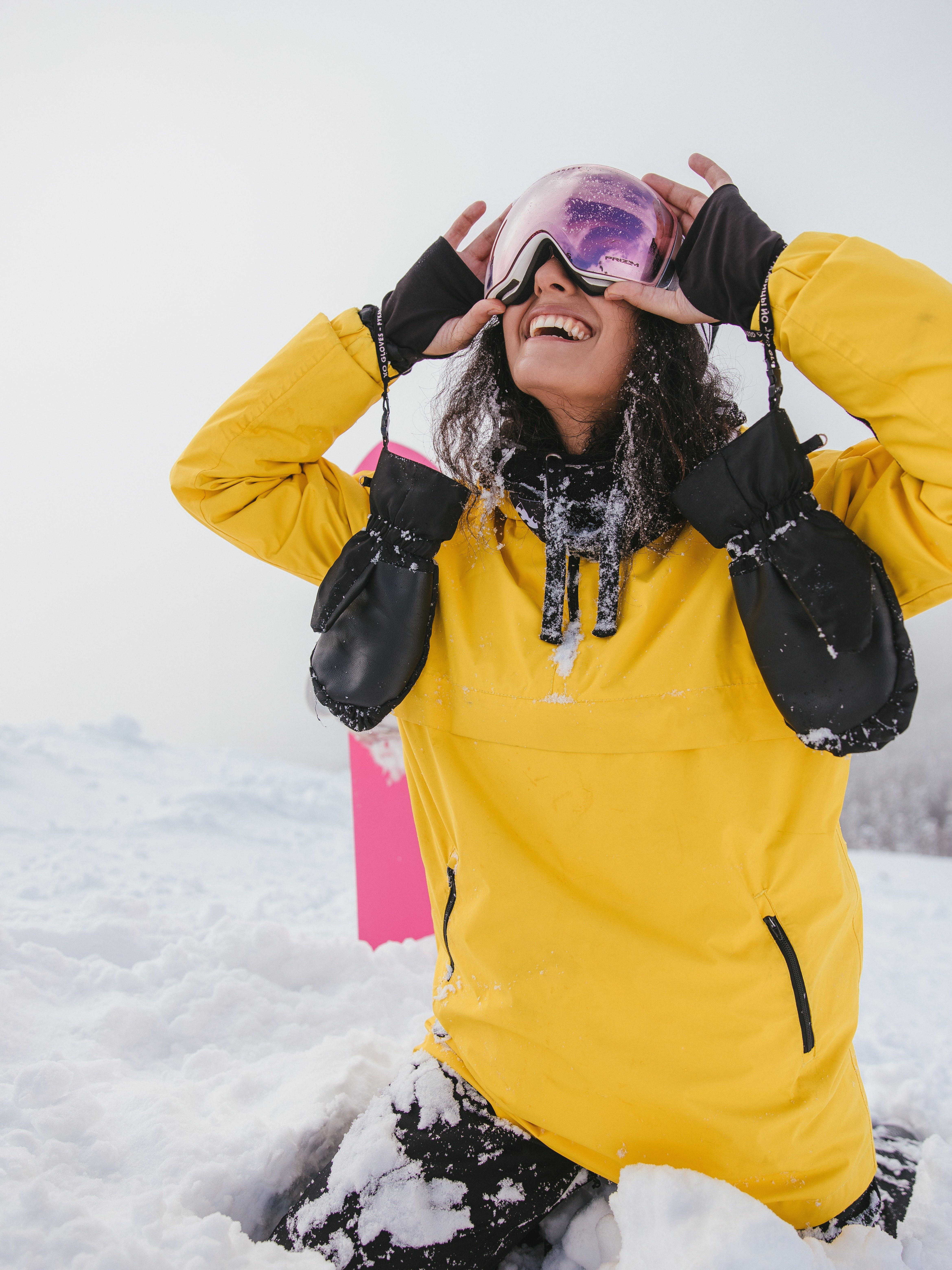Gadis muda sedang bermain ski di musim dingin dengan jaket kuning, snowboard, dan bersenang-senang.