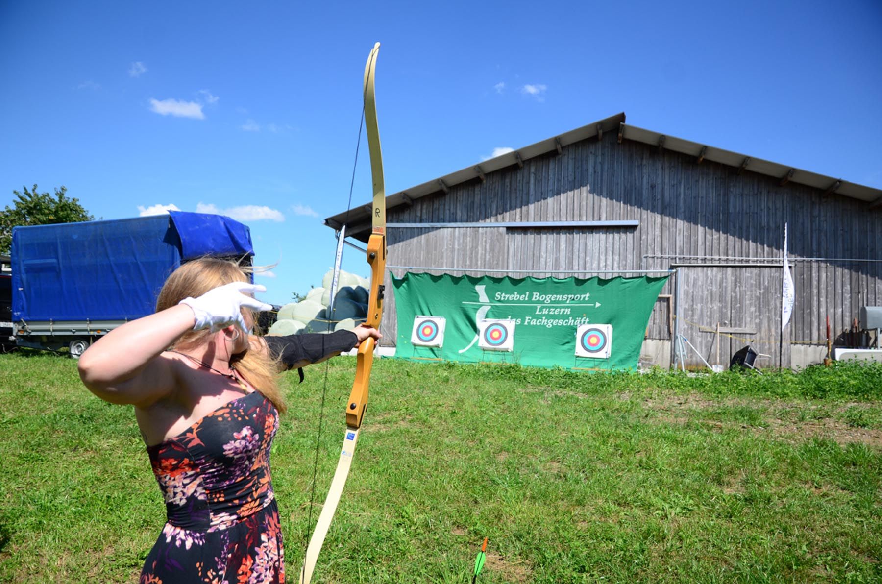 Стрелковая стрельба в Швейцарии: спортсменка стреляет из лука на открытом воздухе, зеленый луг, ясное небо