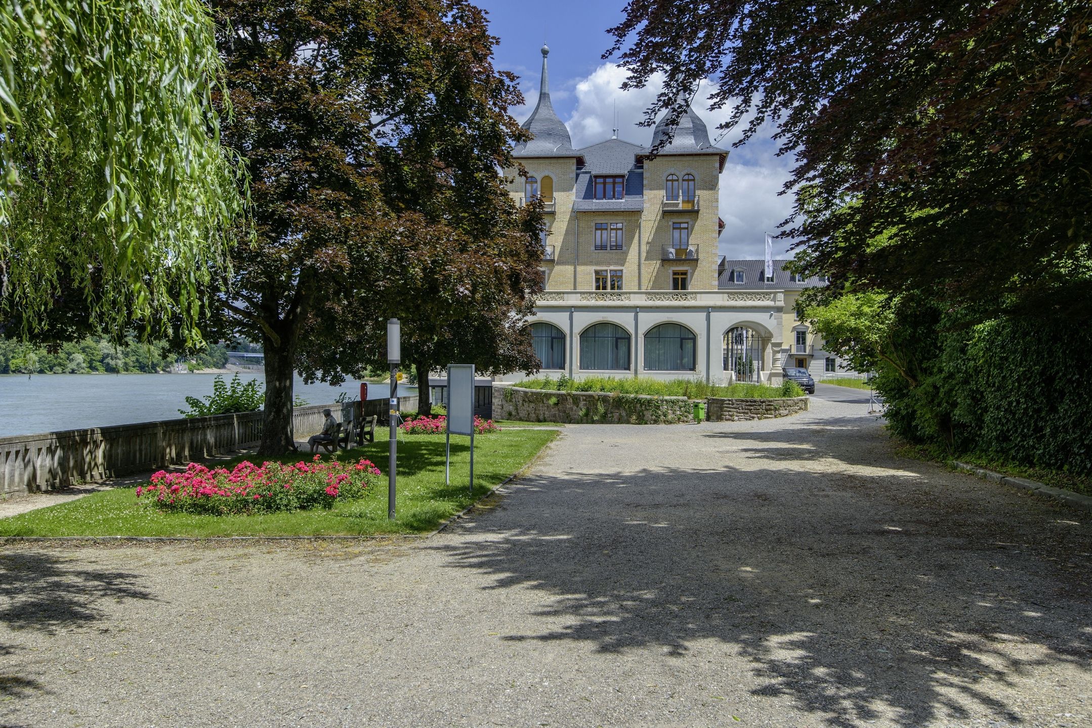 Hotel De Salines am Rheinufer in Rheinfelden mit Blumenbeeten.