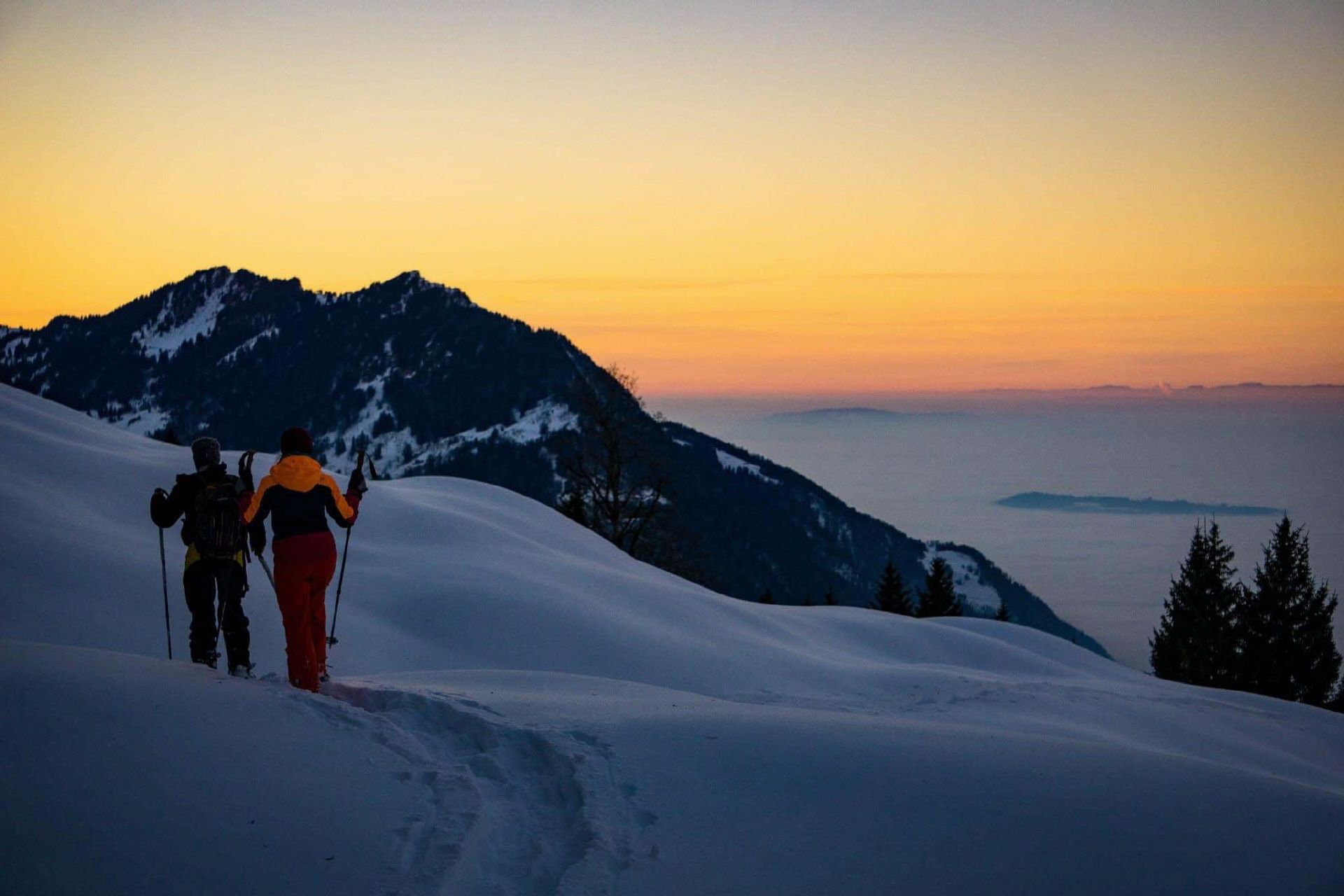 저녁 해가 지는 가운데 두 사람이 케렌저베르크에서 눈신을 신고 하이킹하기