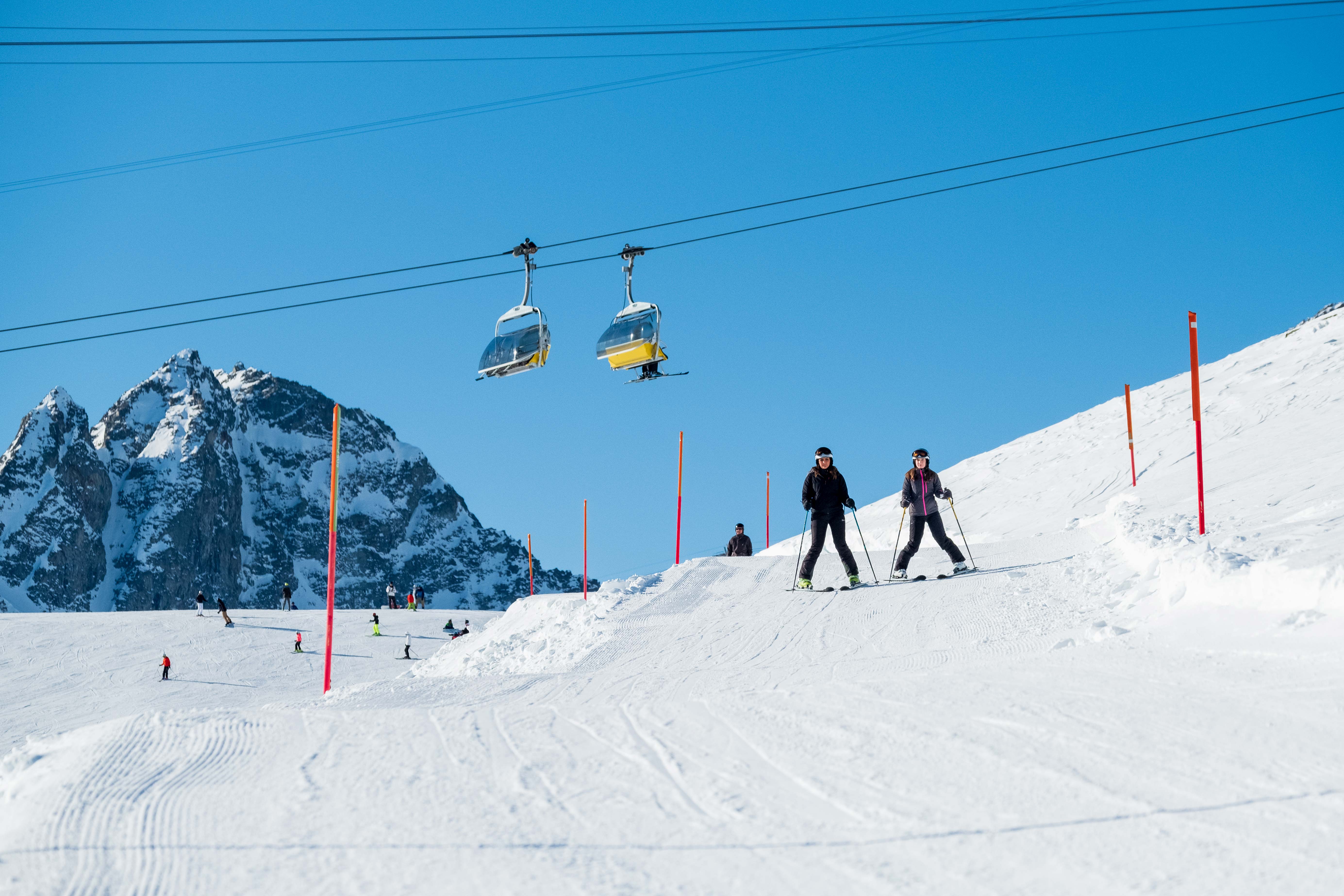 Skileraar op de piste in de winter met bergen op de achtergrond en een lift, ideaal voor sportliefhebbers.