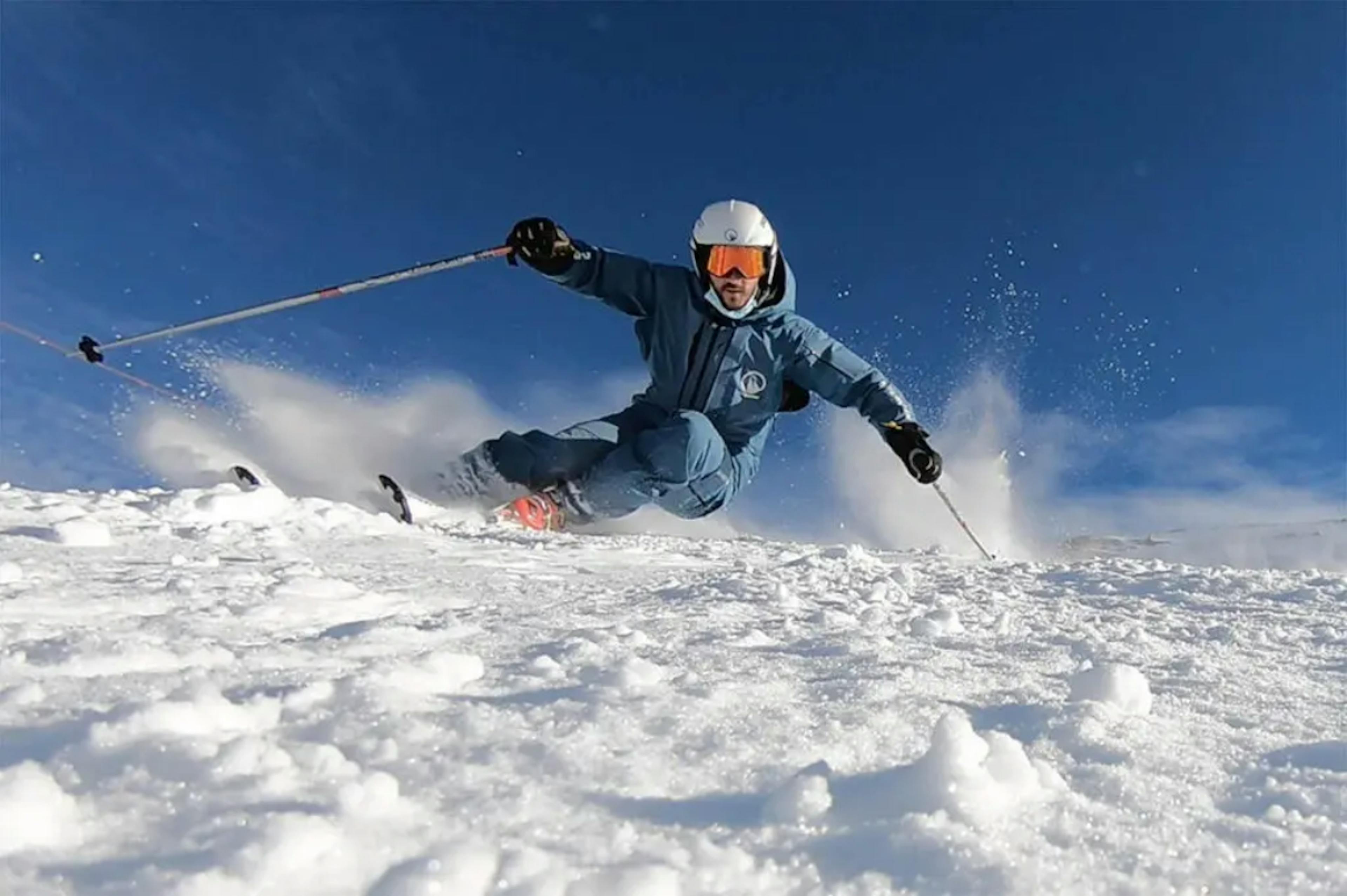 Escuela de esquí: esquiadores con ropa azul haciendo carving en la nieve bajo un cielo azul.