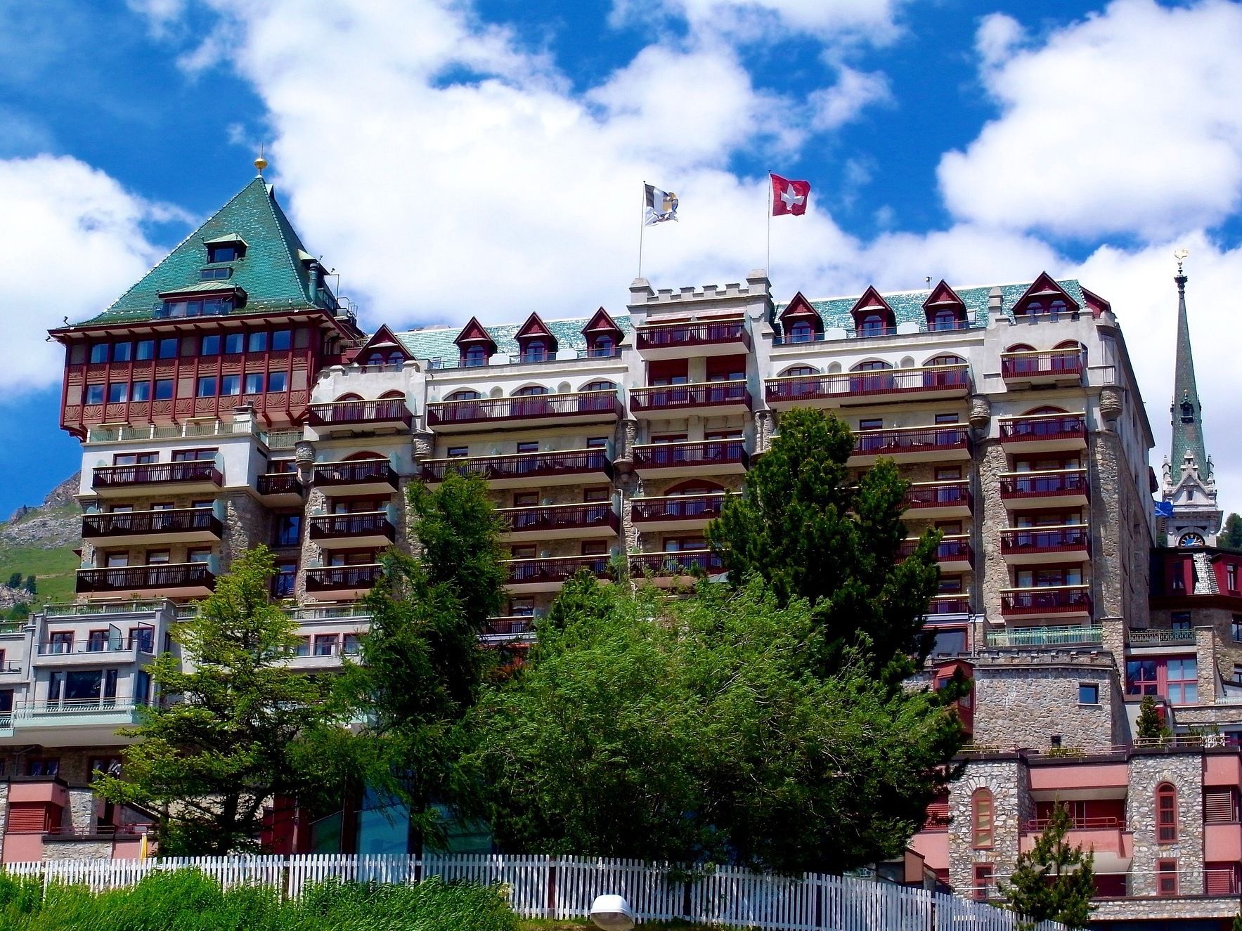 St. Moritz: storslaget hotellbyggnad omgivet av berg och blomstrande natur på sommaren.