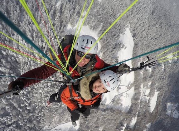 Tandem Gleitschirmflug in Interlaken, Winterlandschaft mit Schnee, zwei Personen in Helmen