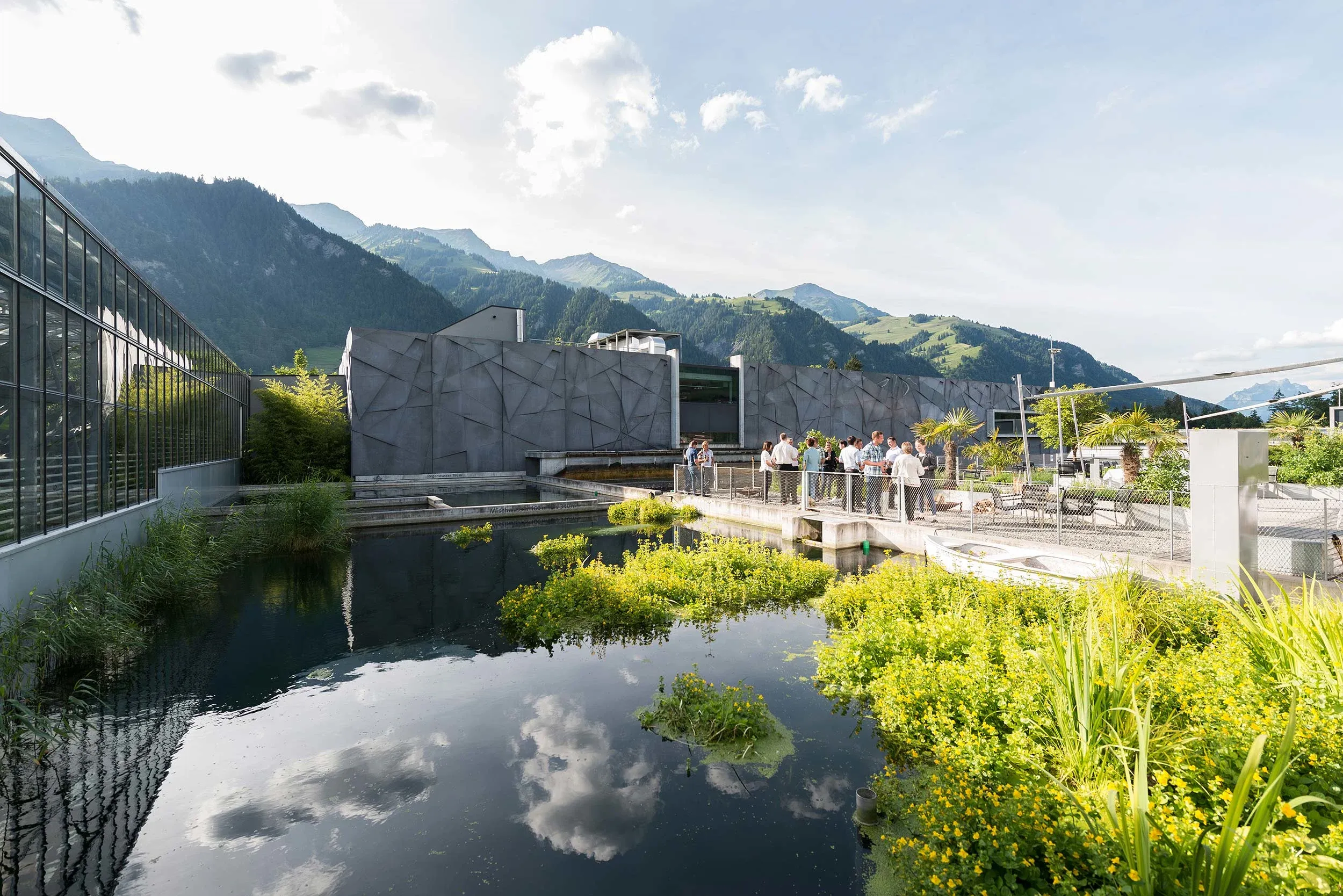 Tropenhaus Frutigen dengan pantulan air dan lingkungan hijau.