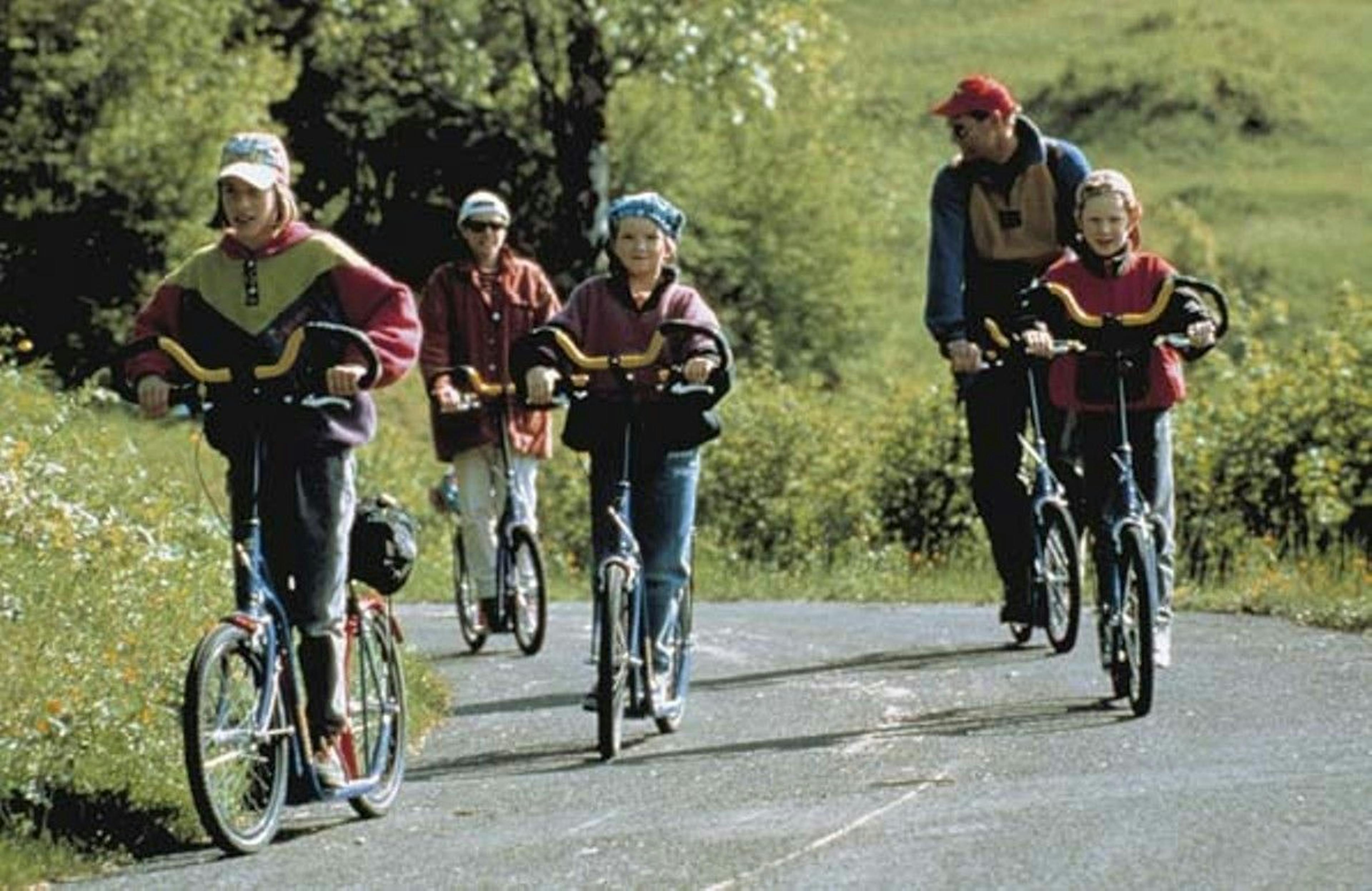 Trottinette in Svizzera su una tranquilla strada di campagna, circondata da prati verdi e alberi.