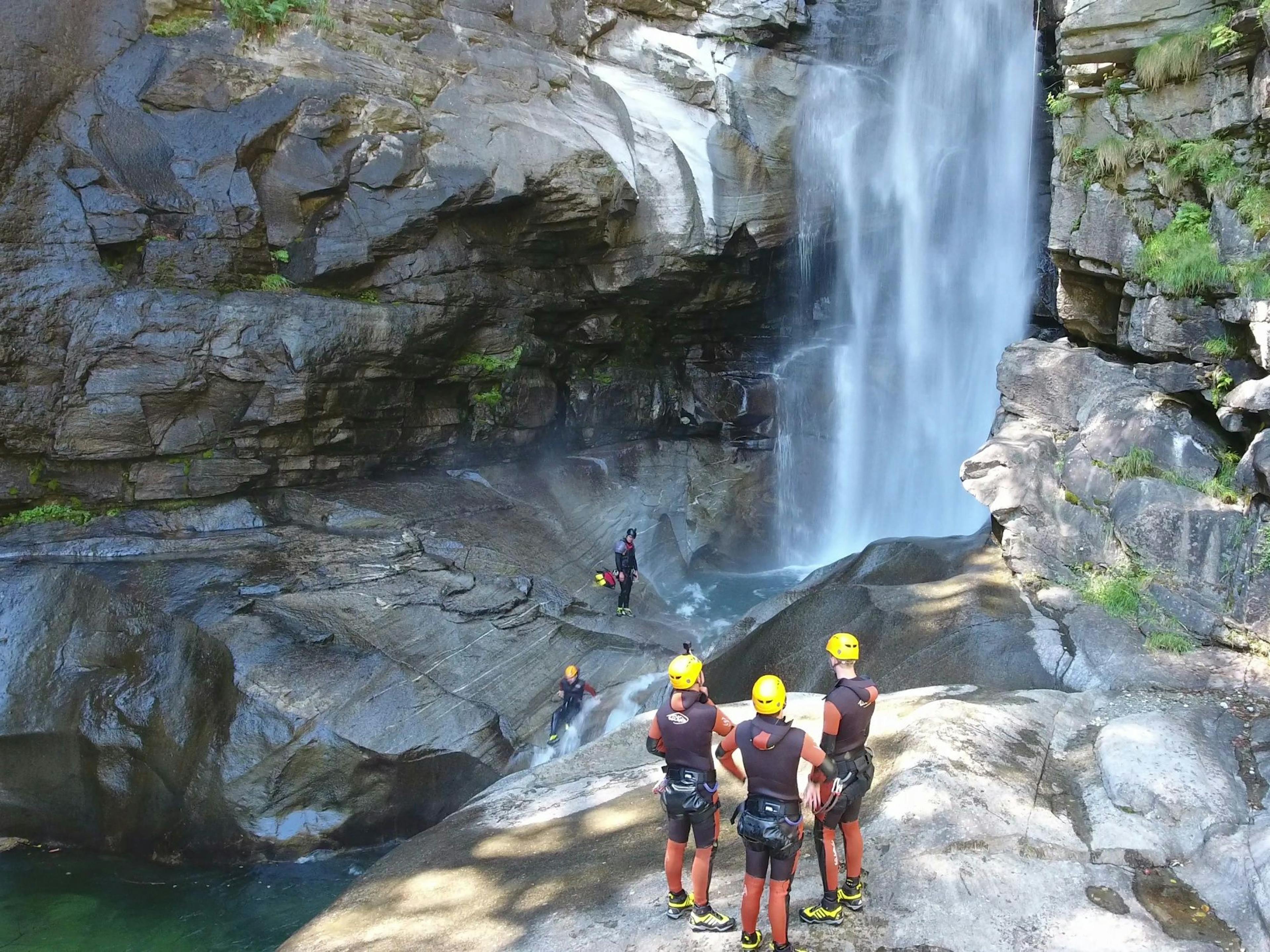 Heli Canyoning: Group in front of a waterfall in the canyon, adventurous activities in nature.