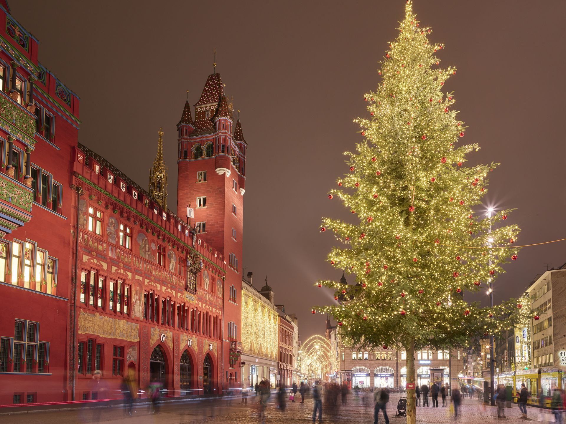 Maravillas de Navidad en Basilea con un árbol de Navidad iluminado y el histórico ayuntamiento de fondo por la noche.